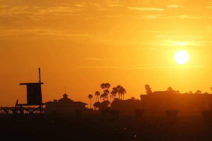 Outline of lifeguard station, palm trees with orange-yellow sunset sky behind
